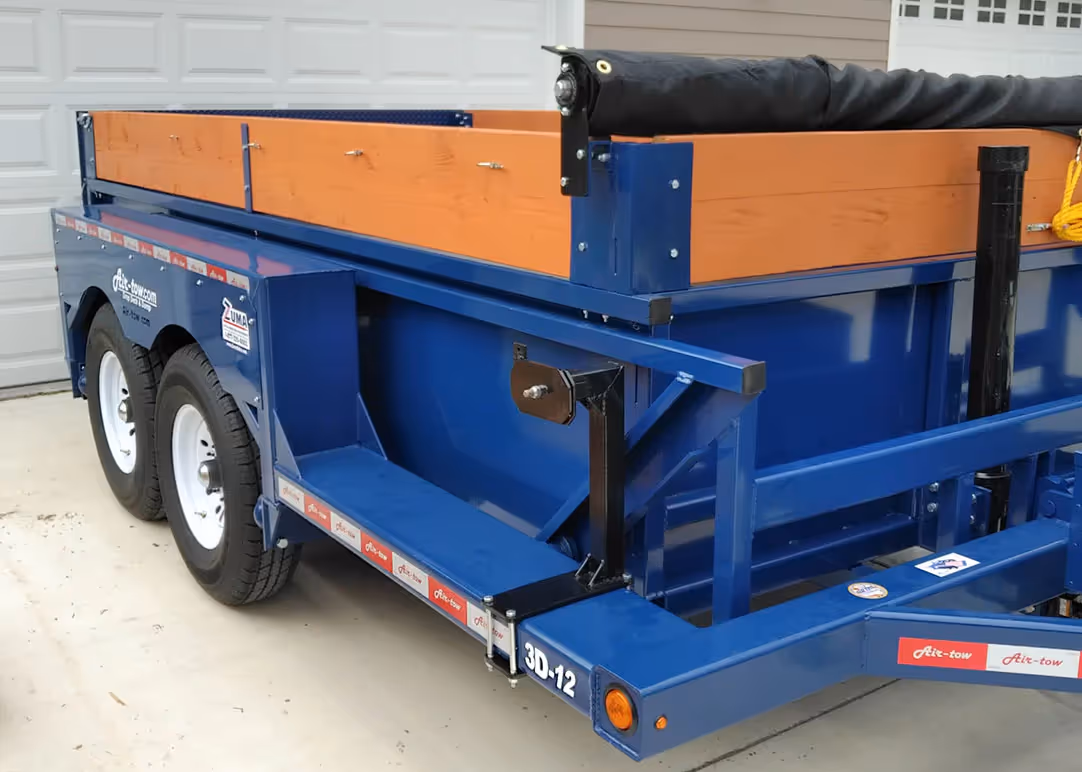 Rear quarter view of the Air-Tow 3D-12 dump trailer, highlighting the dual-axle wheels and wooden side extenders.