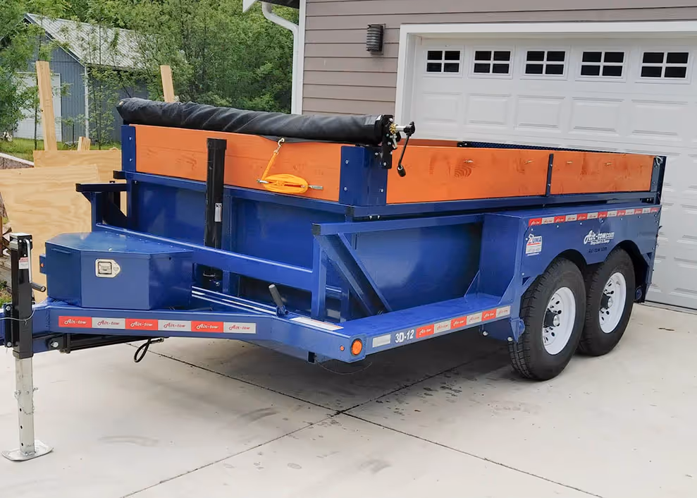 Clean side profile of the Air-Tow 3D-12 dump trailer parked on a concrete driveway, showing the jack and toolbox.