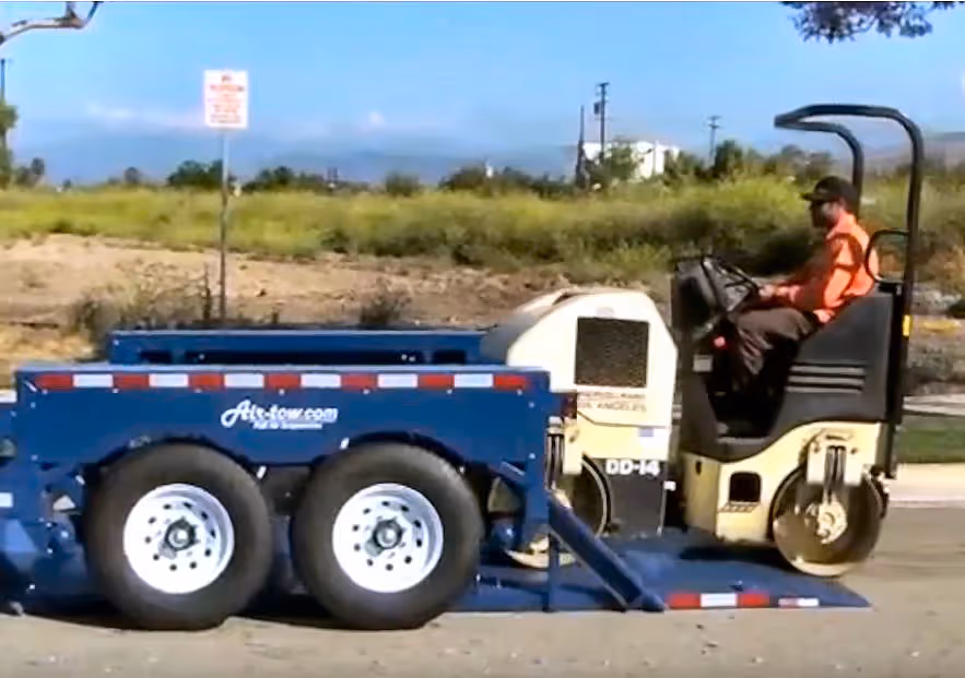 A road roller easily driving off a blue Air-Tow drop deck trailer, showcasing simple equipment unloading.