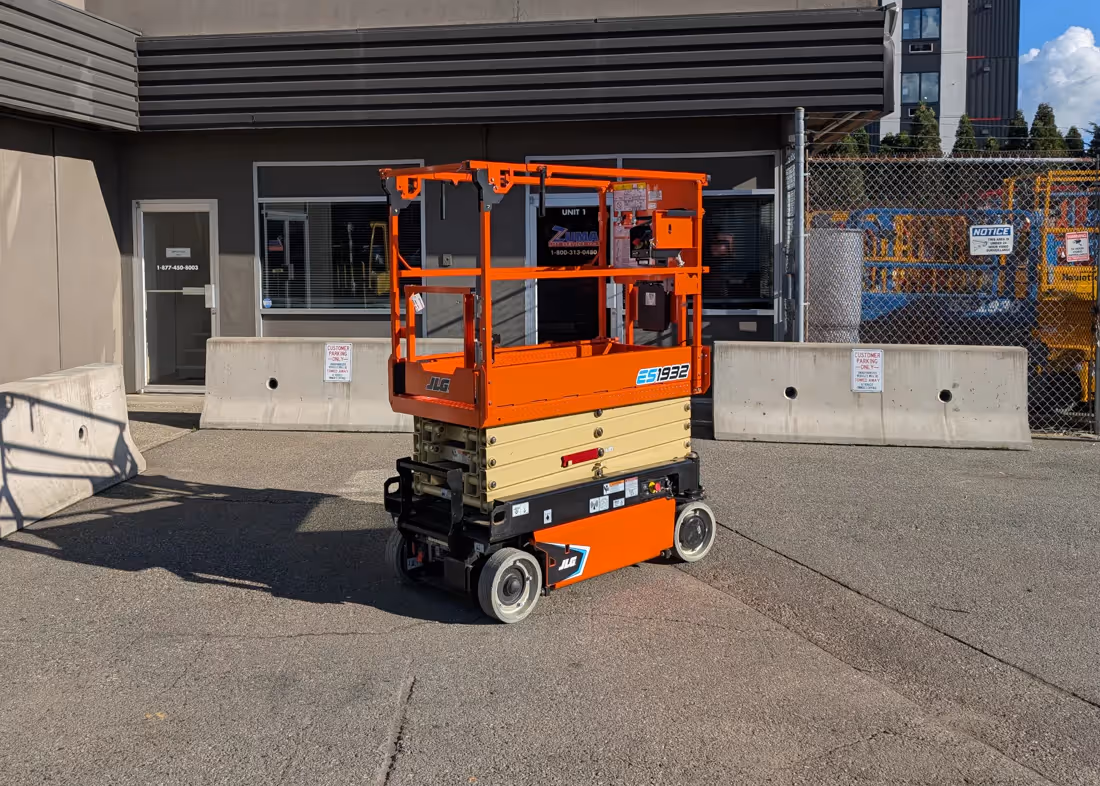 JLG ES1932 electric scissor lift in its stowed position parked on pavement outside a service building.
