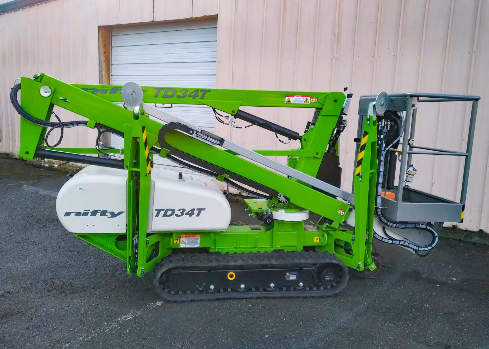 Niftylift TD34T track boom lift side view parked outside an industrial building