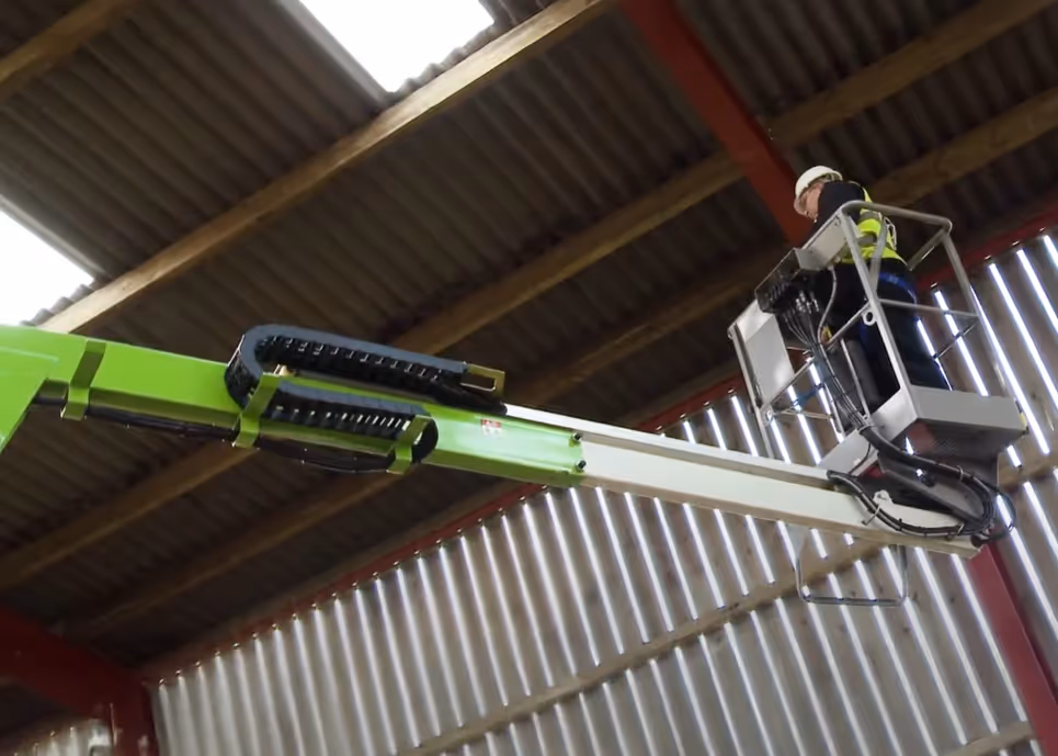 Operator using a Niftylift TD34T track boom lift with the boom extended inside a warehouse.