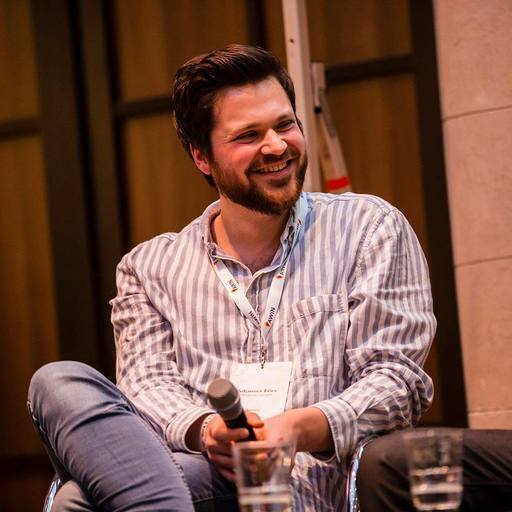 Smiling man with beard in a striped shirt holding a microphone during a discussion.