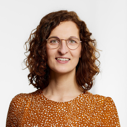 Woman with curly brown hair wearing glasses and an orange patterned top smiling at the camera.