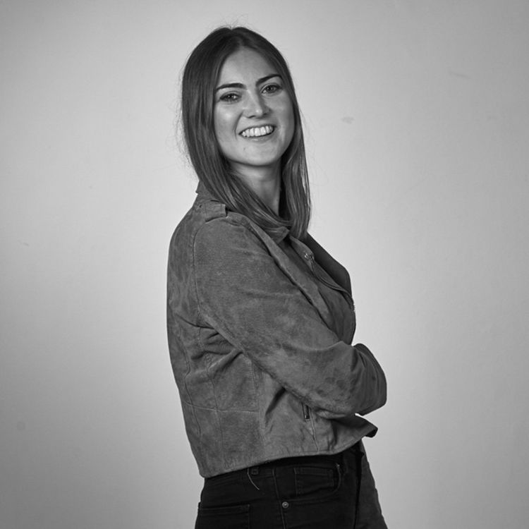 Smiling woman with straight hair wearing a suede jacket and black pants, posing with arms crossed against a plain background.