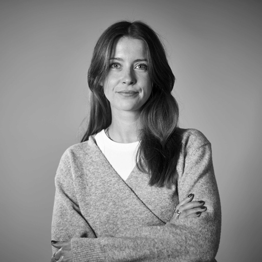 Black and white portrait of a woman with long hair wearing a light sweater, standing with arms crossed and smiling slightly.
