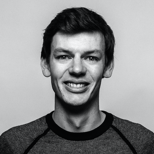 Black and white portrait of a smiling young man with short dark hair wearing a textured shirt.