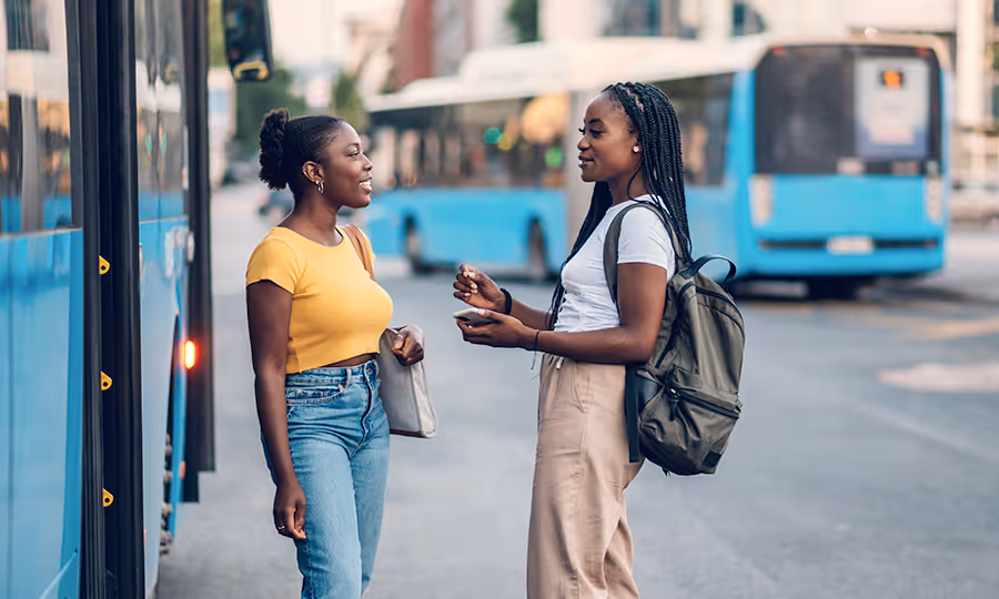 two college student talk standing in front of transit bus 