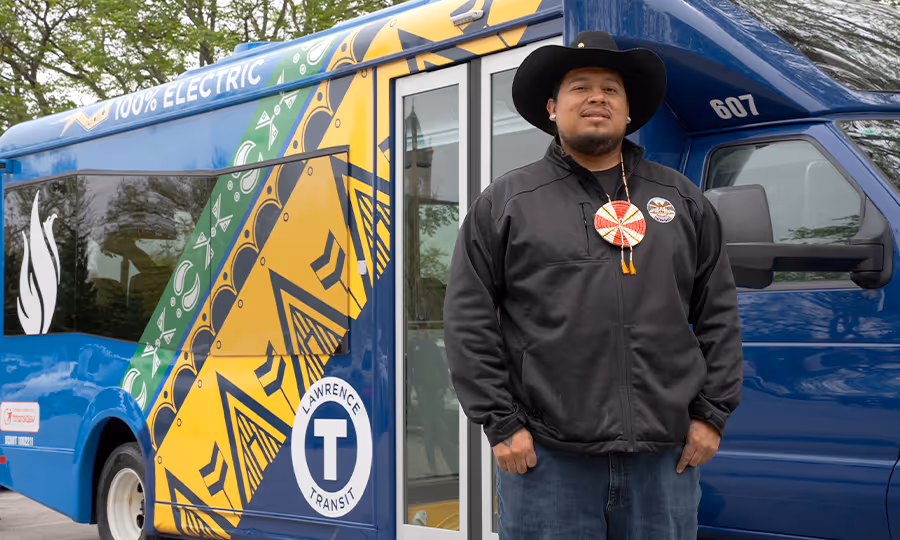 Man in wide brimmed hat stands in front of shuttle bus with bright pattern on side