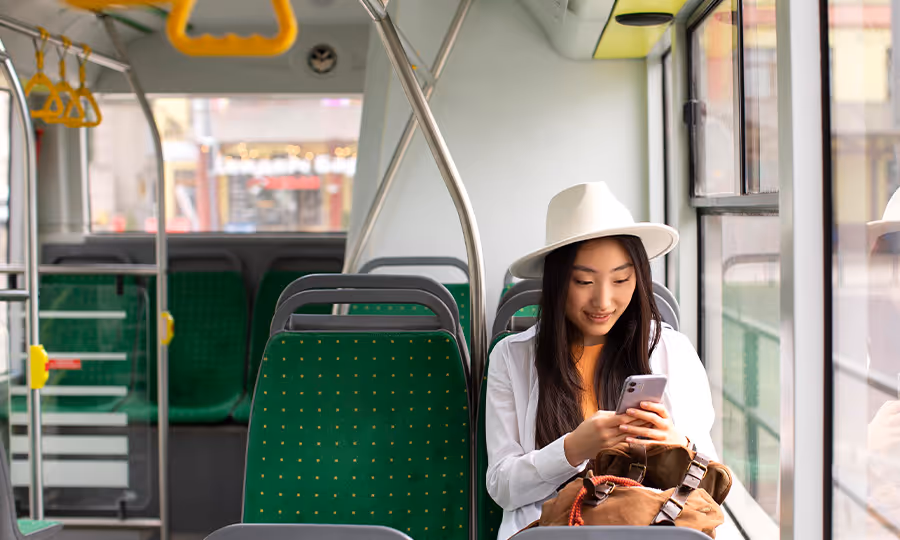 young woman rides empty transit bus and looks happily at her phone 