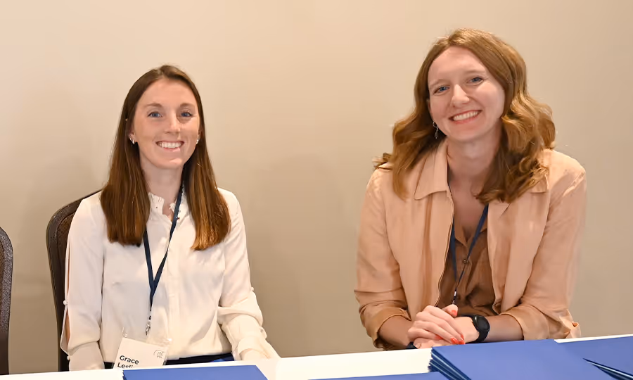 Two female CTE staff members sit behind registration table and smile at camera