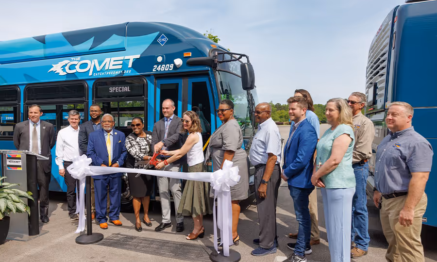 A small group of people stand in front of ribbon posing for camera at new transit bus ceremony for COMET transit. 