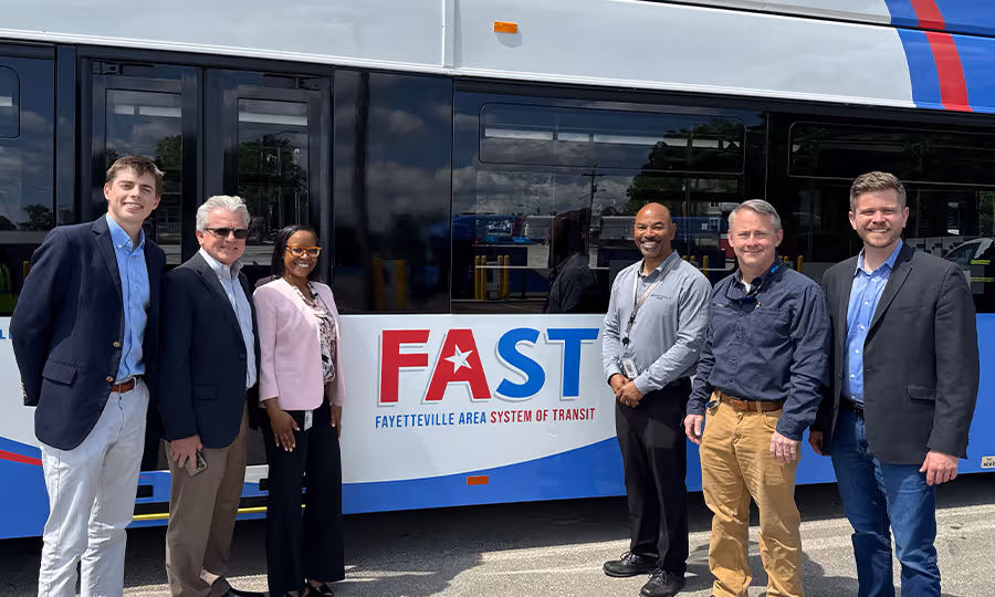 Six people stand in front of FAST transit bus and smile during ribbon cutting ceremony