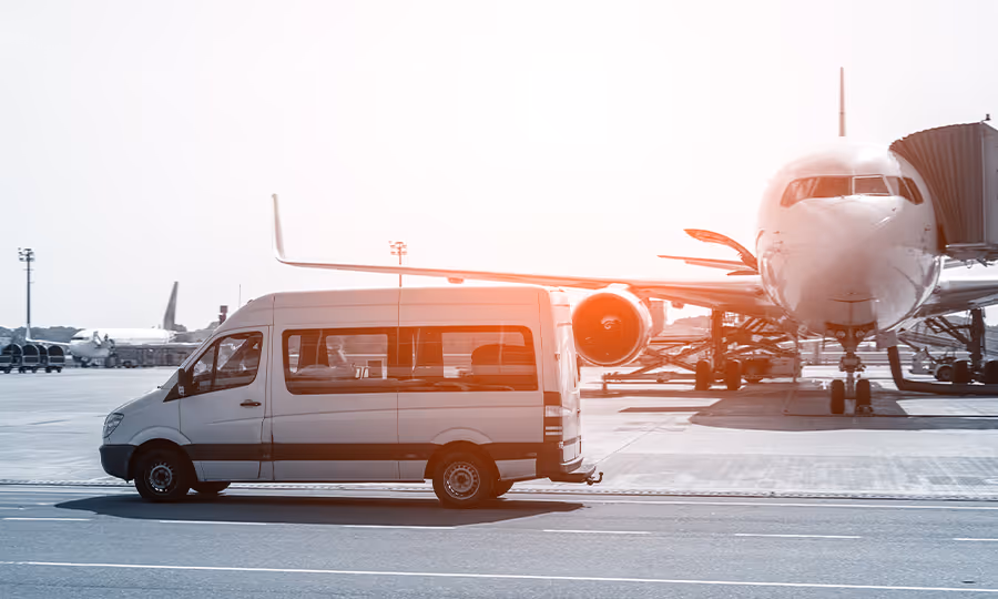 shuttle van driving on airport tarmac with airplane in background