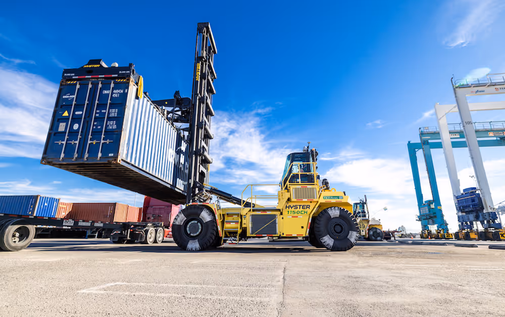 large fork lift top loader moving shipping container across dock yard