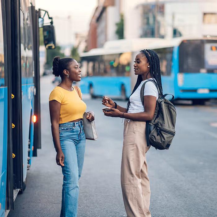 two college students stand and talk near transit bus