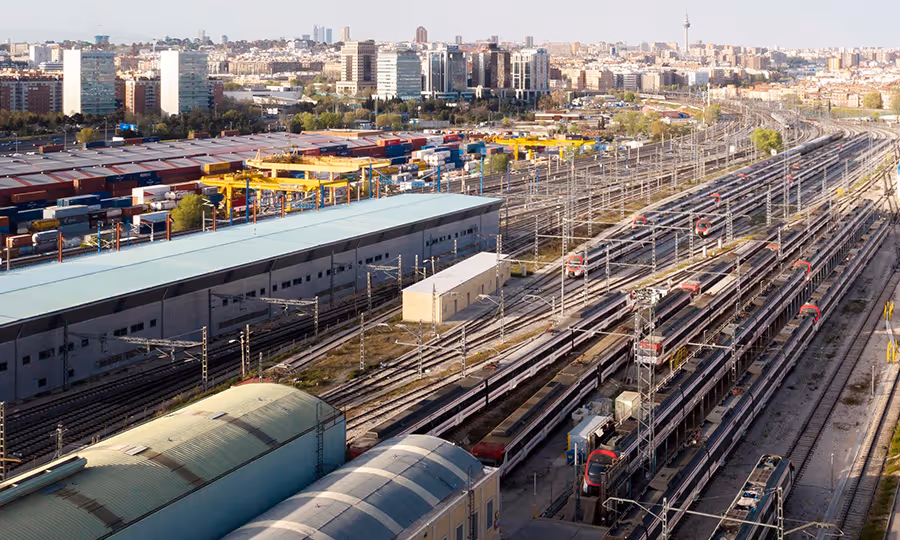 overview of busy train station with many vehicles and lines running with a metropolitan city in background