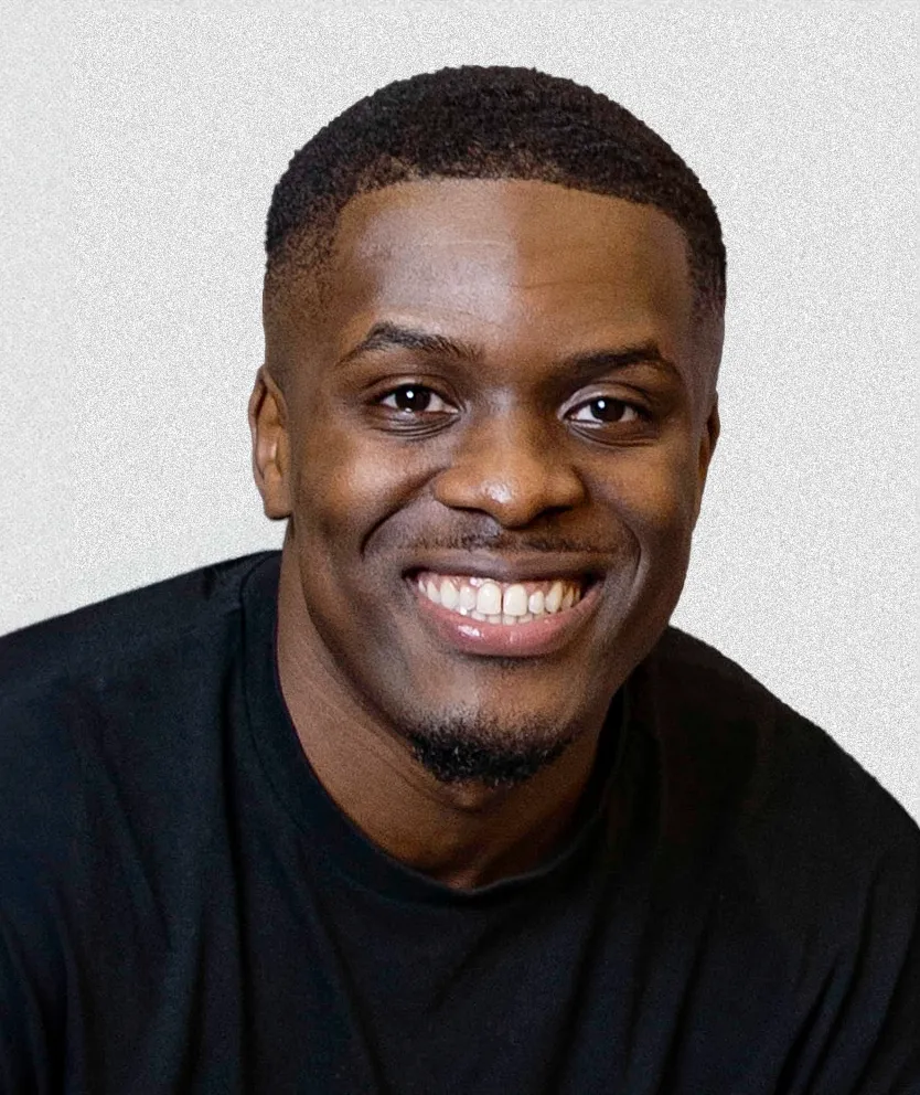 Smiling young man with short hair and goatee wearing a black shirt against a light background.
