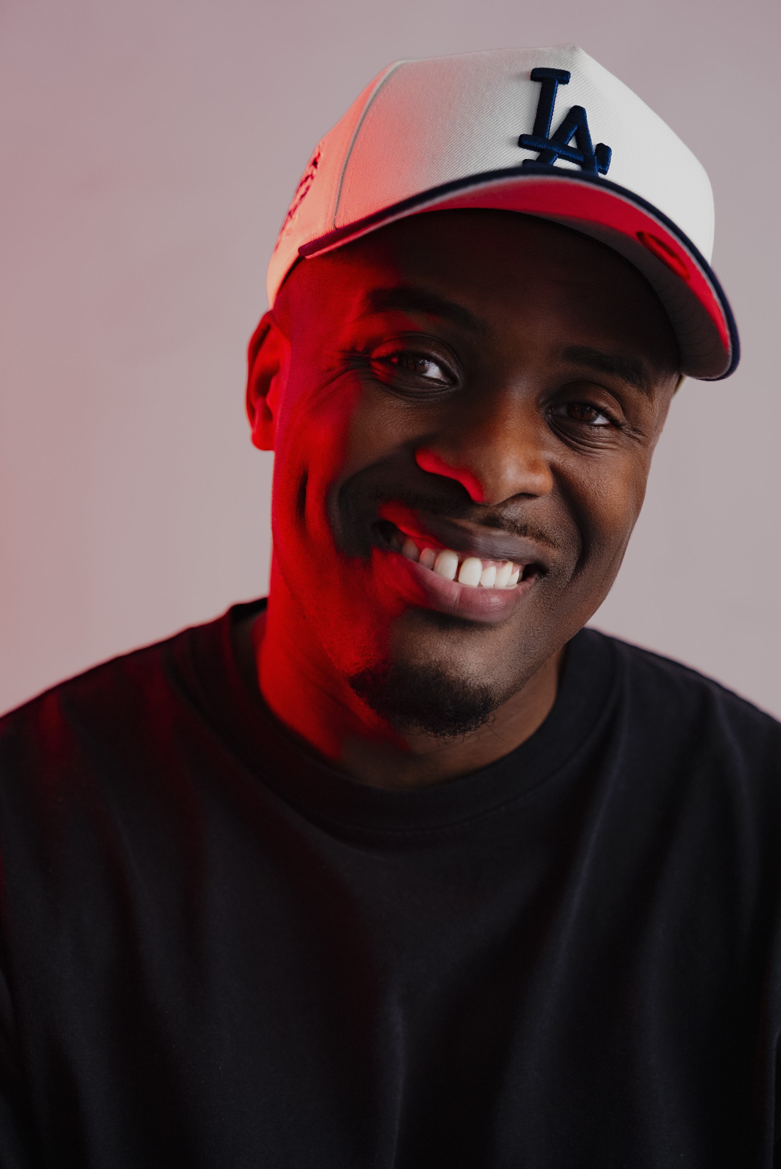 Smiling young man with short hair and goatee wearing a black shirt against a light background.