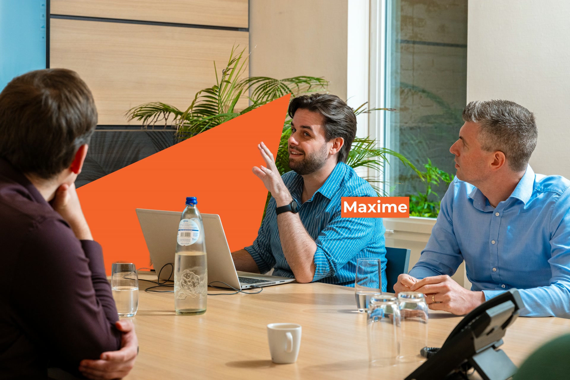 Maxime legt iets uit aan collega's tijdens een teamvergadering in een moderne kantoorruimte.