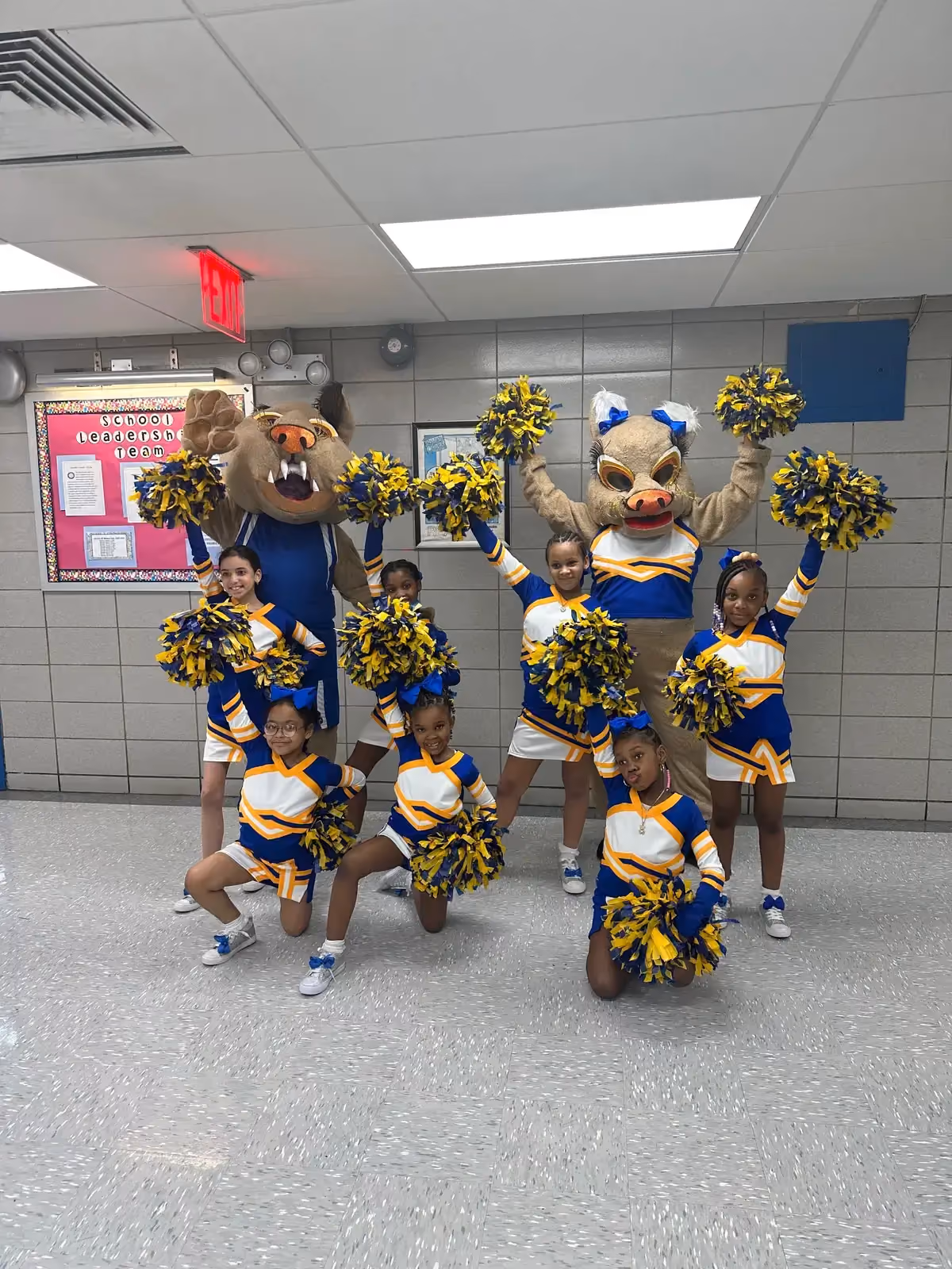 Student cheerleaders posing with school mascots holding blue and gold pom-poms