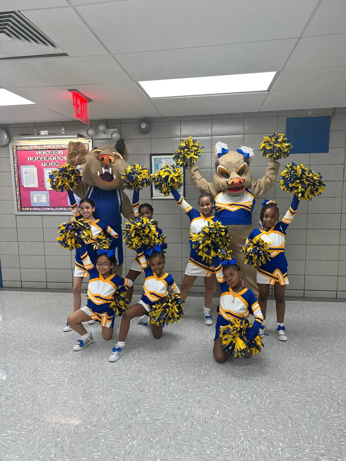 Student cheerleaders posing with school mascots holding blue and gold pom-poms