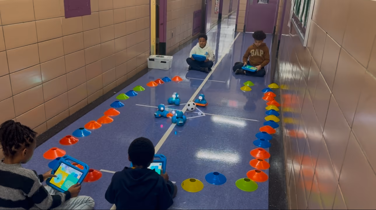 Students using tablets to program a Dash robot in school hallway