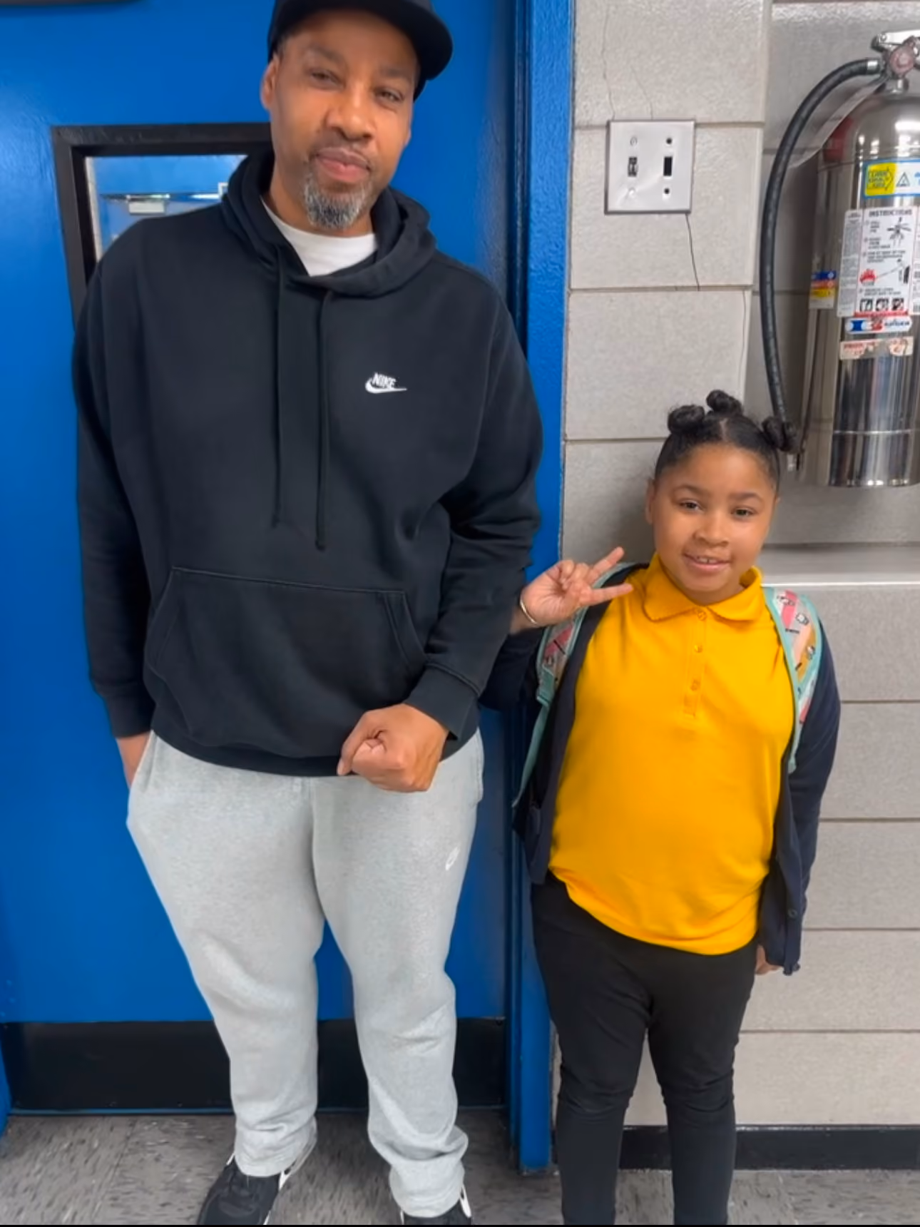 Adult and smiling student with backpack posing in school hallway