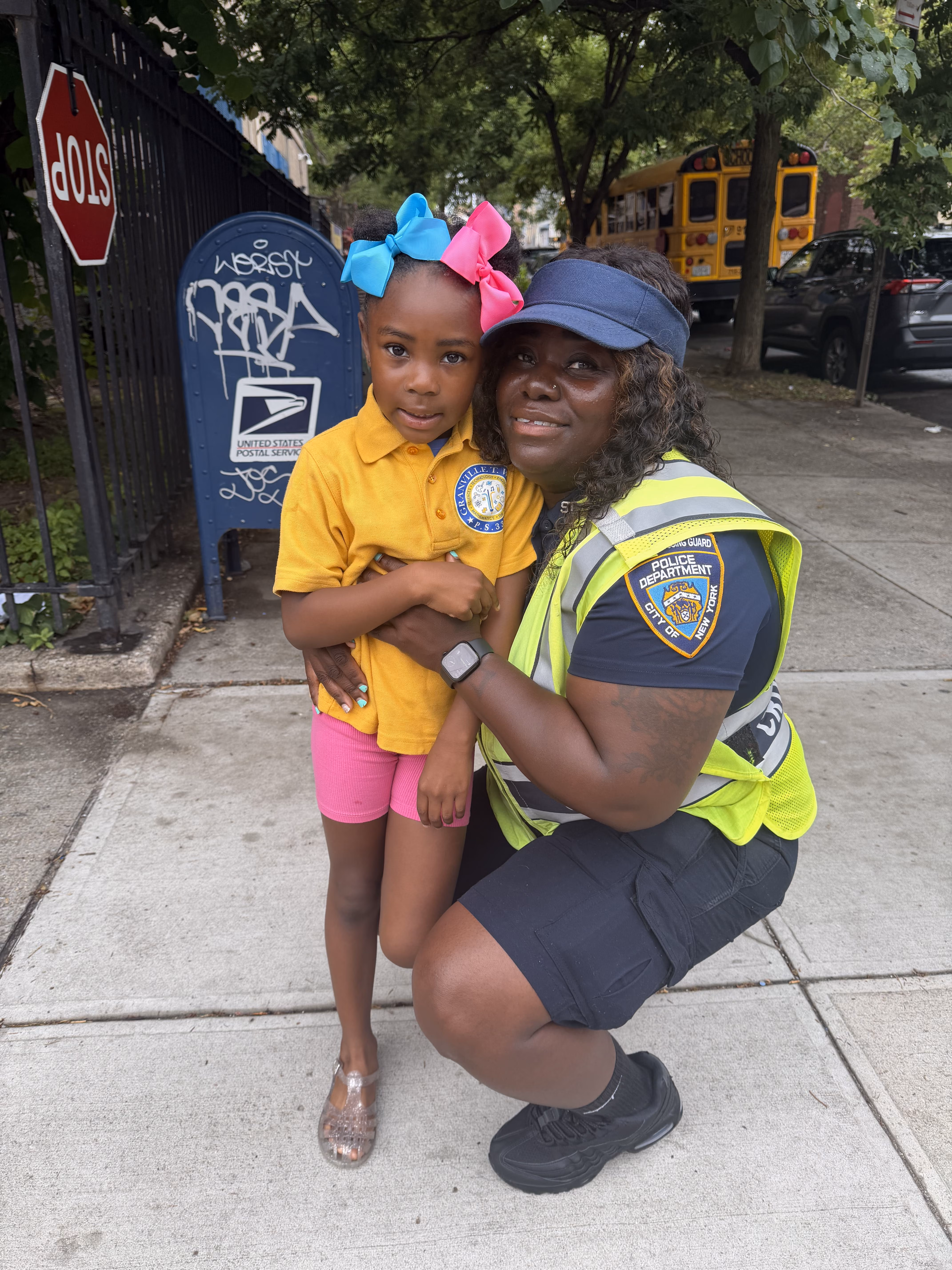 NYPD crossing guard kneeling with young student near school bus