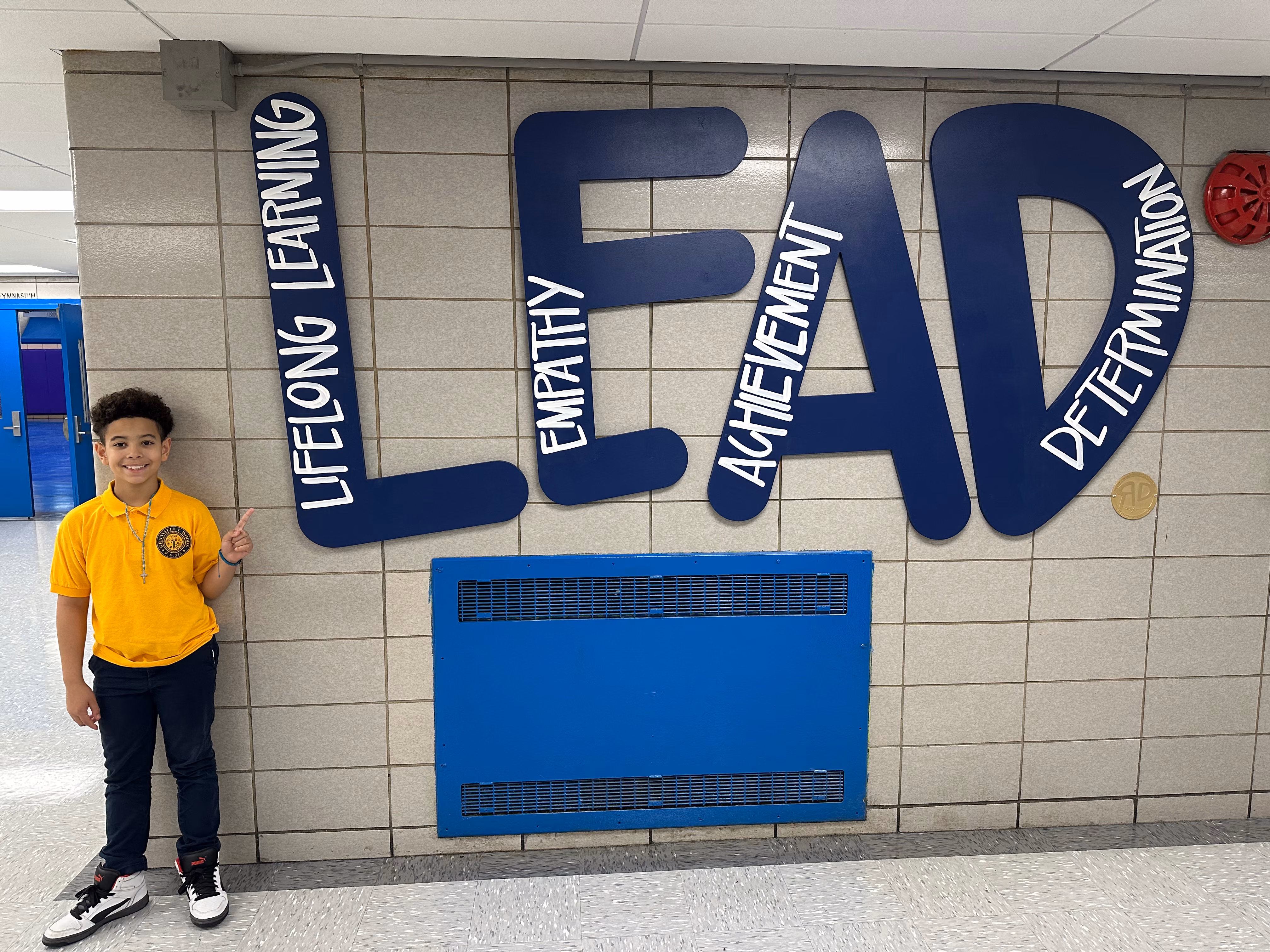 Student giving thumbs up beside LEAD core values hallway mural