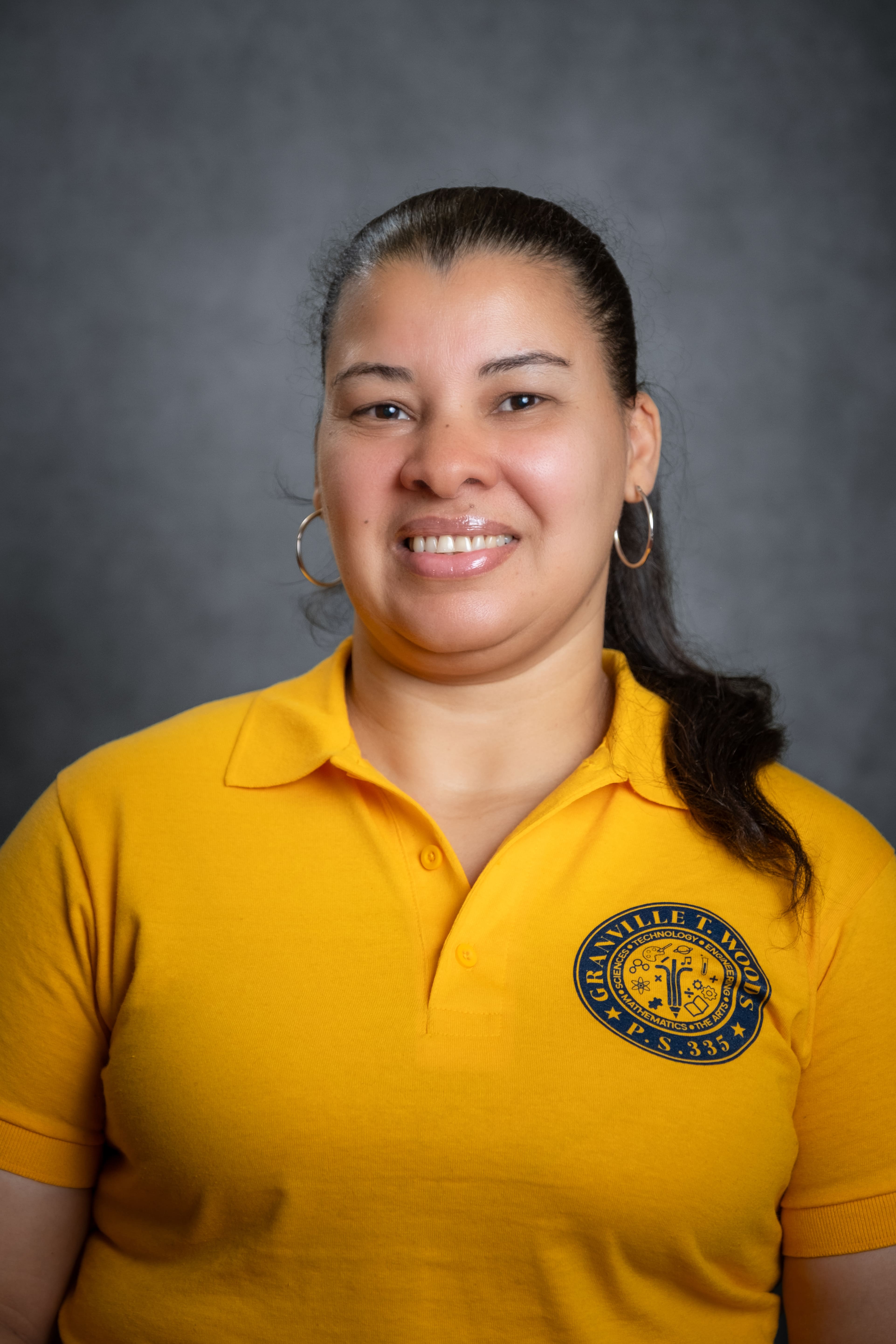 Staff member C. Quezada smiling in PS 335 school polo shirt