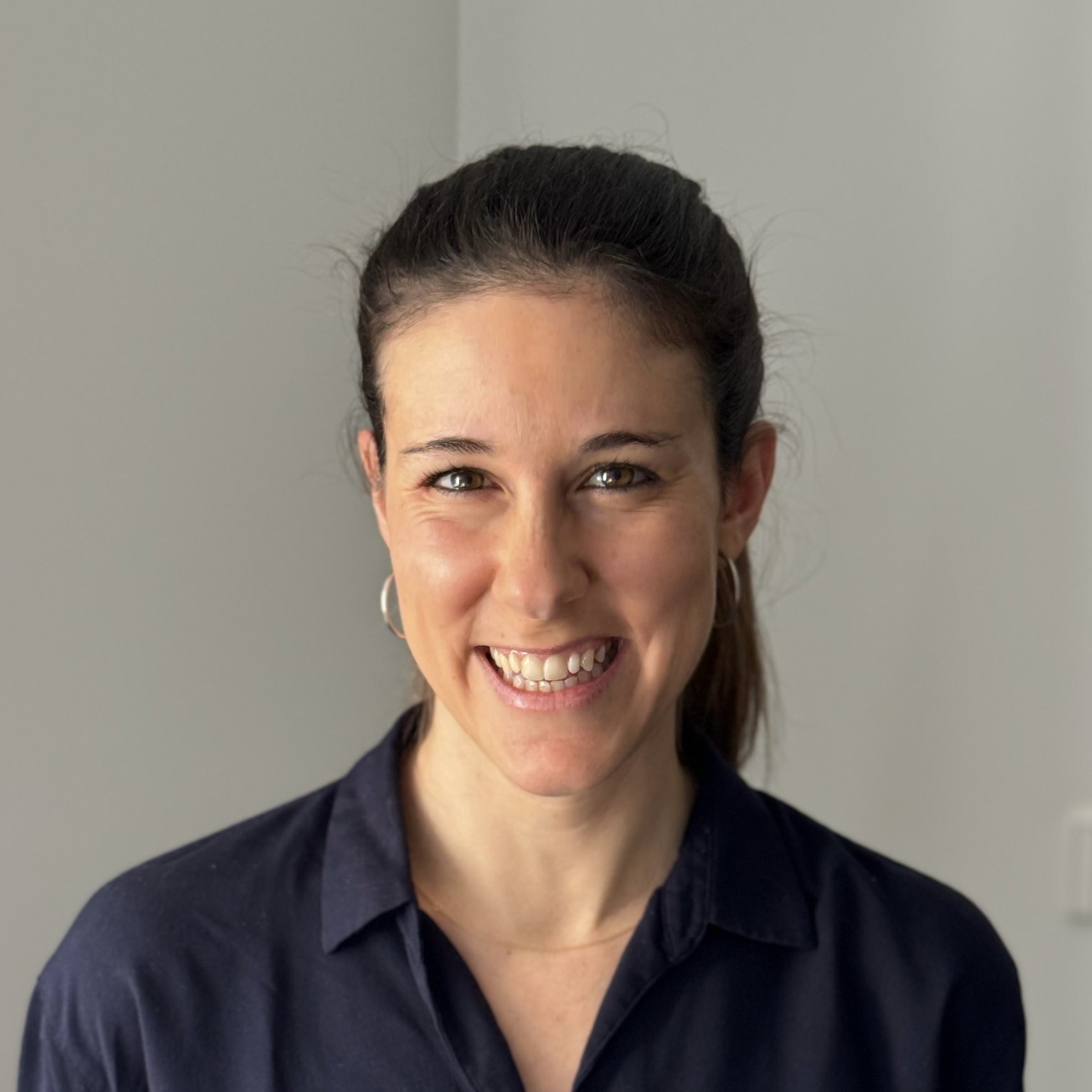 Donna sorridente con capelli raccolti e camicia blu su sfondo grigio neutro.