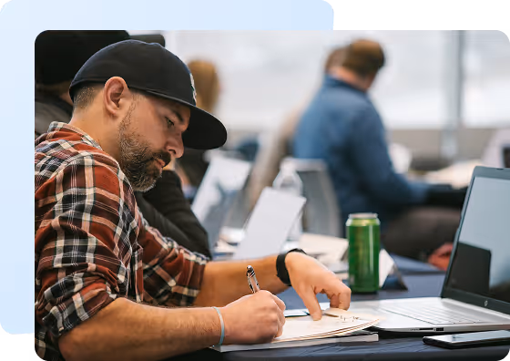A group photo of three men sitting on stairs, all wearing matching black JobNimbus T-shirts. They are positioned side by side, smiling and posing in front of a house with a simple wooden background.