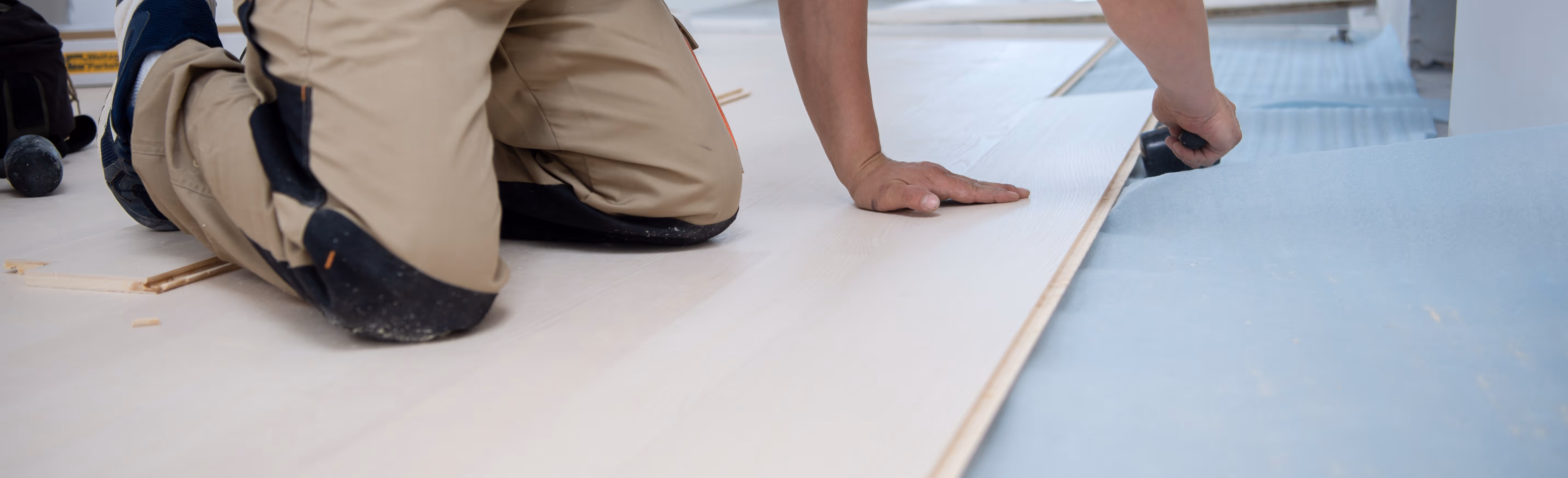 A flooring installer measuring wood planks he's installing