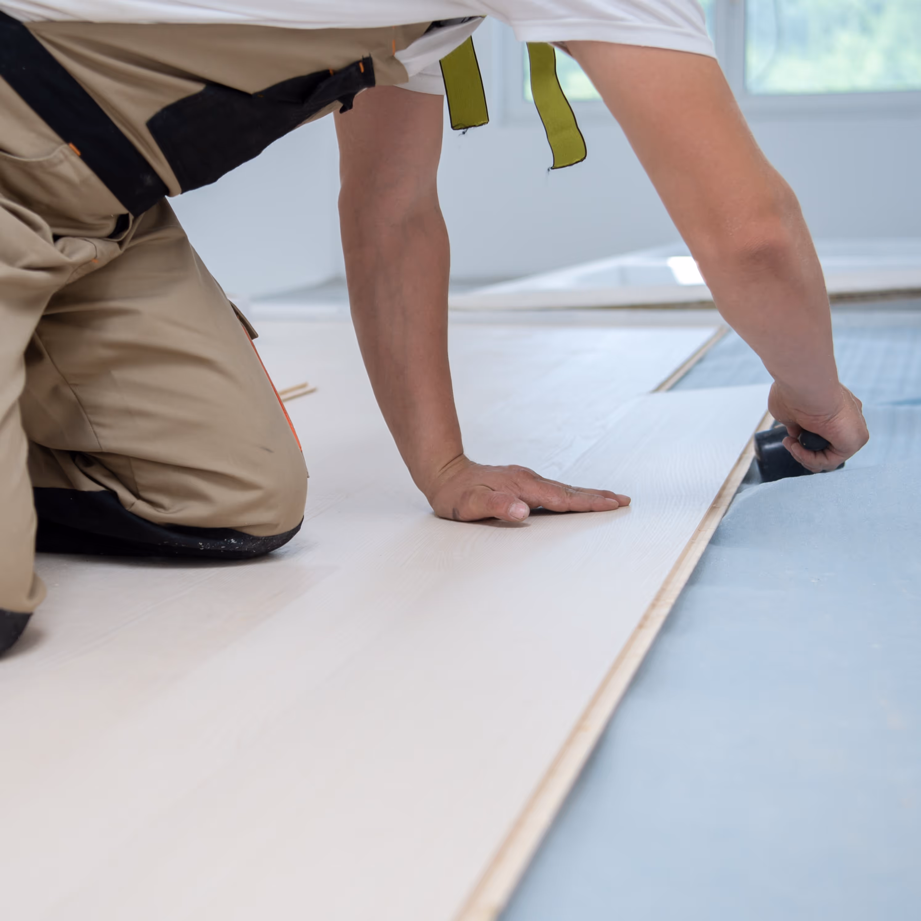 A flooring installer measuring wood planks he's installing - Mobile sized image