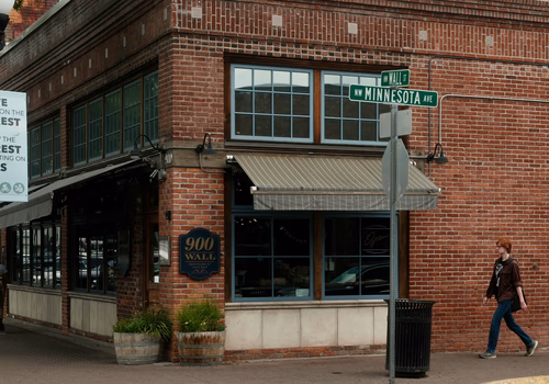 Brick corner building with a sign reading '900 Wall' and street signs for Wall St and Minnesota Ave, with a person walking on the sidewalk.