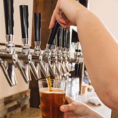 Person pouring amber beer from a tap into a glass at a bar.