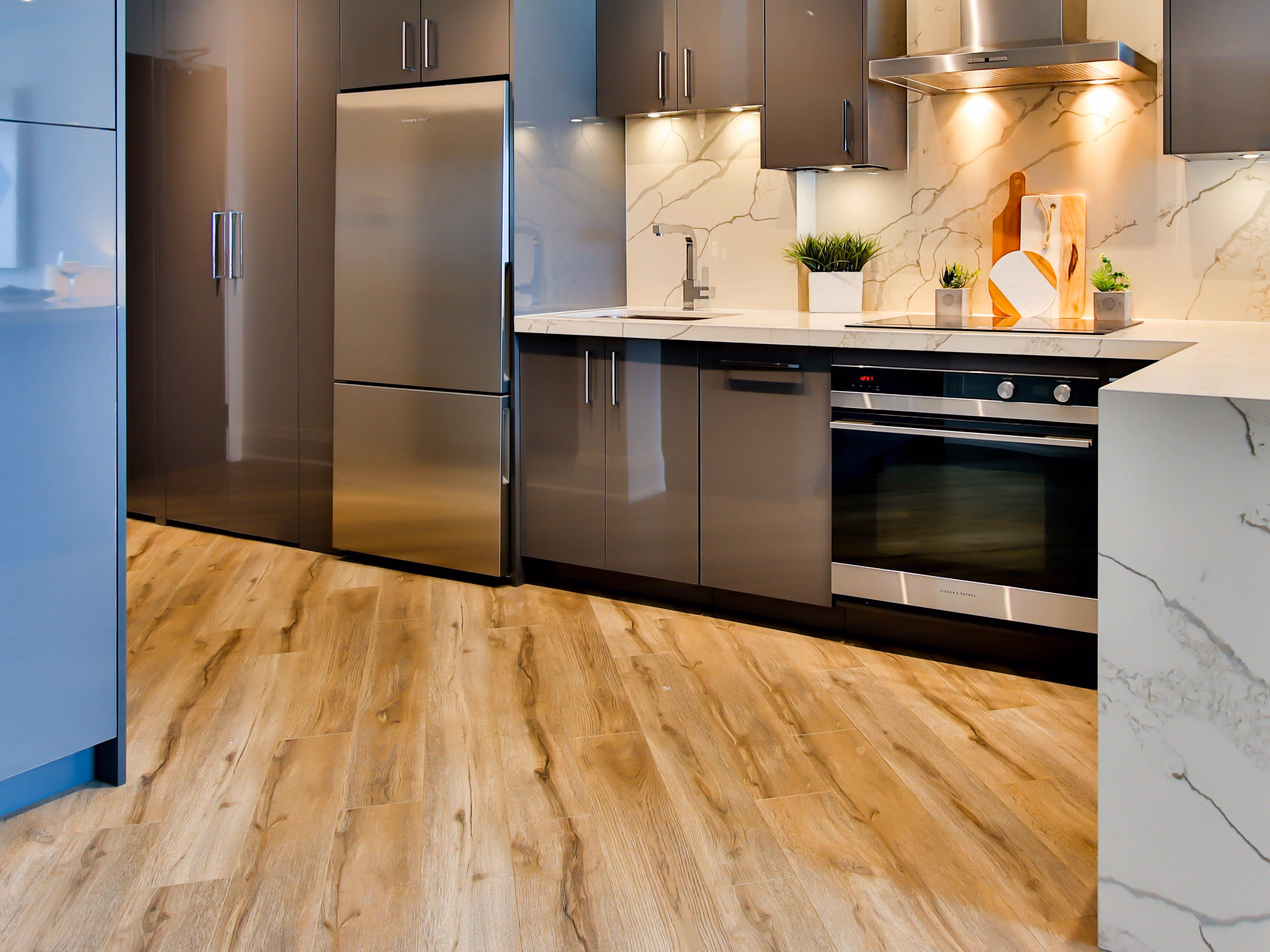 Modern kitchen with stainless steel refrigerator, oven, gray cabinets, marble backsplash, and wood-look flooring.