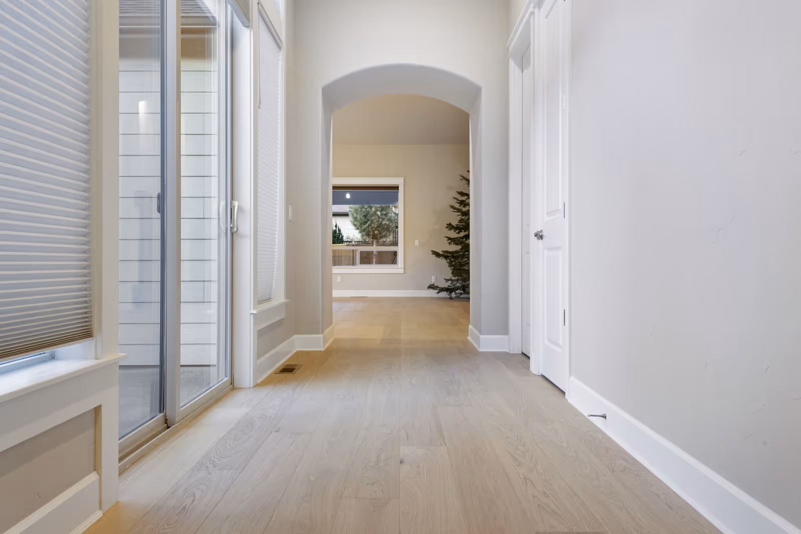 Bright hallway with light wood flooring, white walls, an arched doorway, and sliding glass doors on the left.