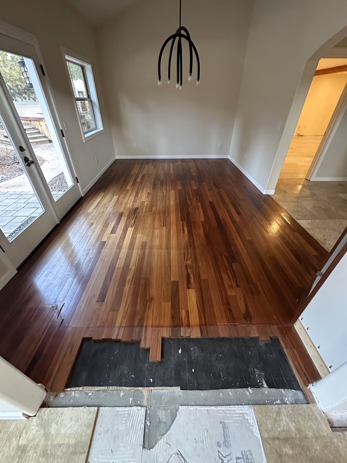 Room with partially installed dark hardwood flooring leading to tile flooring attached to the kitchen.