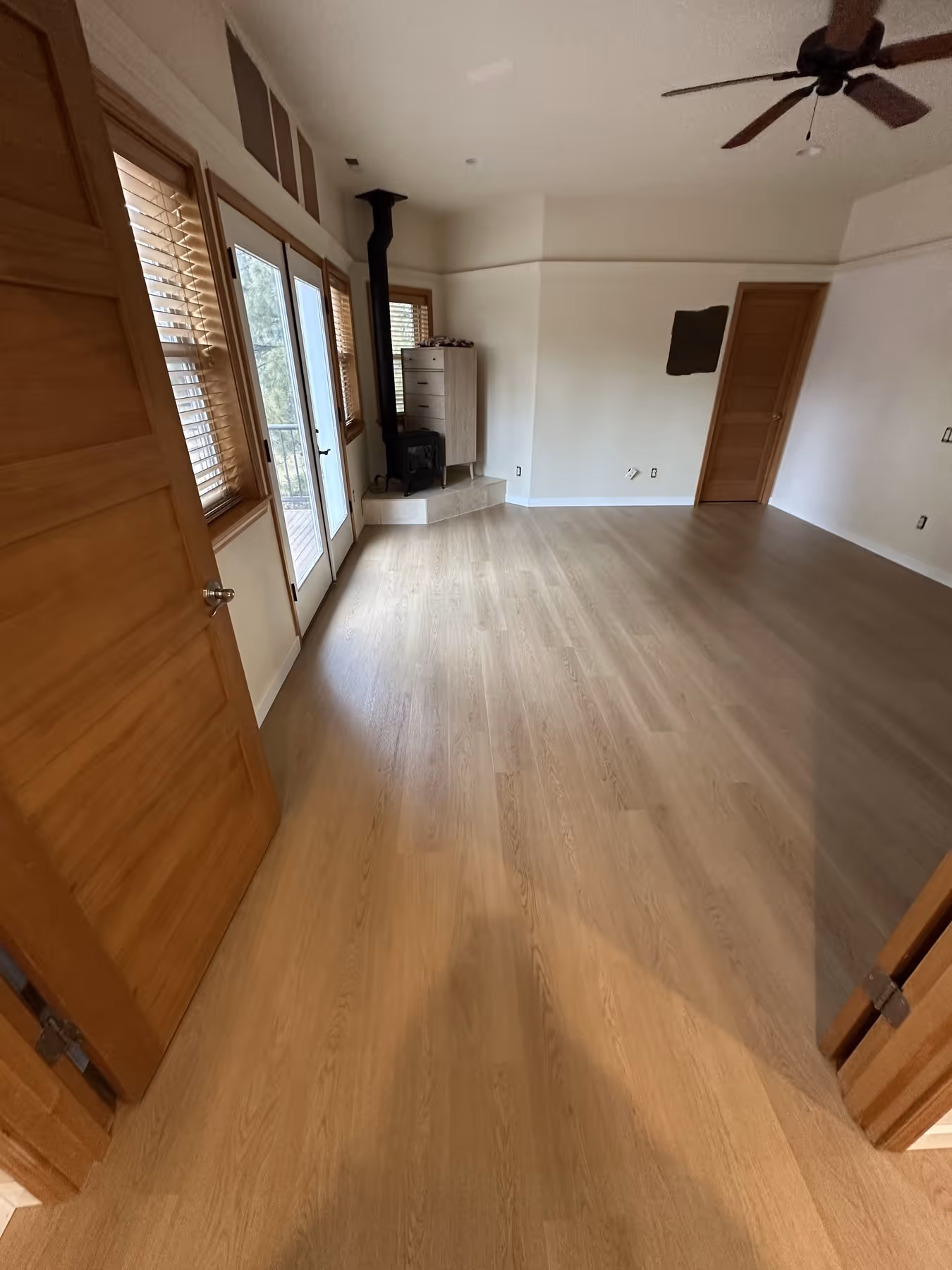 Empty room with light LVP floor, wood stove on tiled platform, multiple windows and wooden doors.
