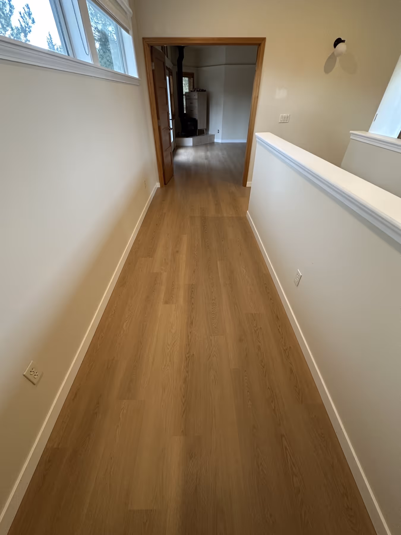 Narrow hallway with light LVP flooring, white walls, a window on the left, and an open door leading to another room.