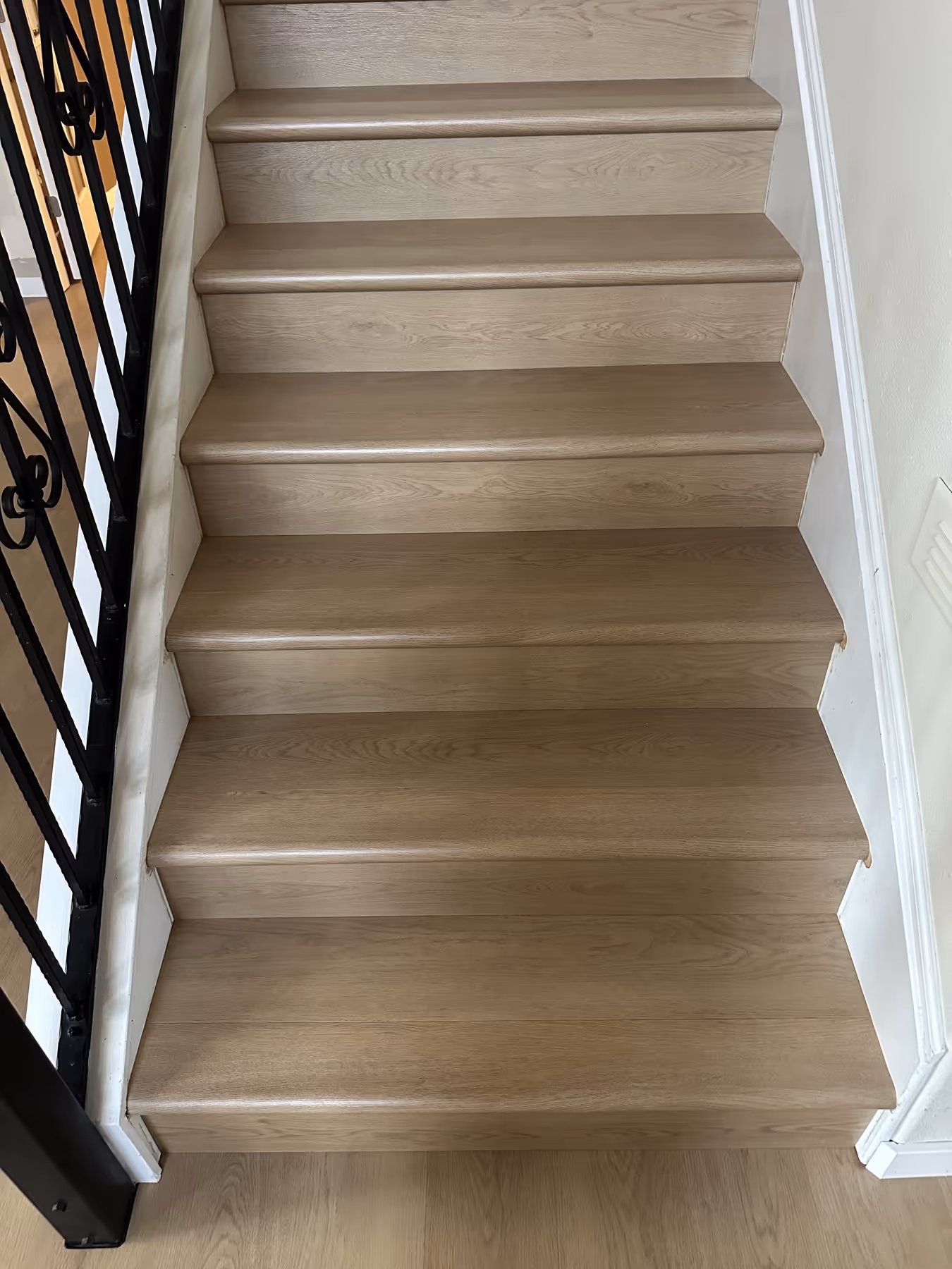 Light LVP flooring staircase with six steps and black metal railing on the left side.