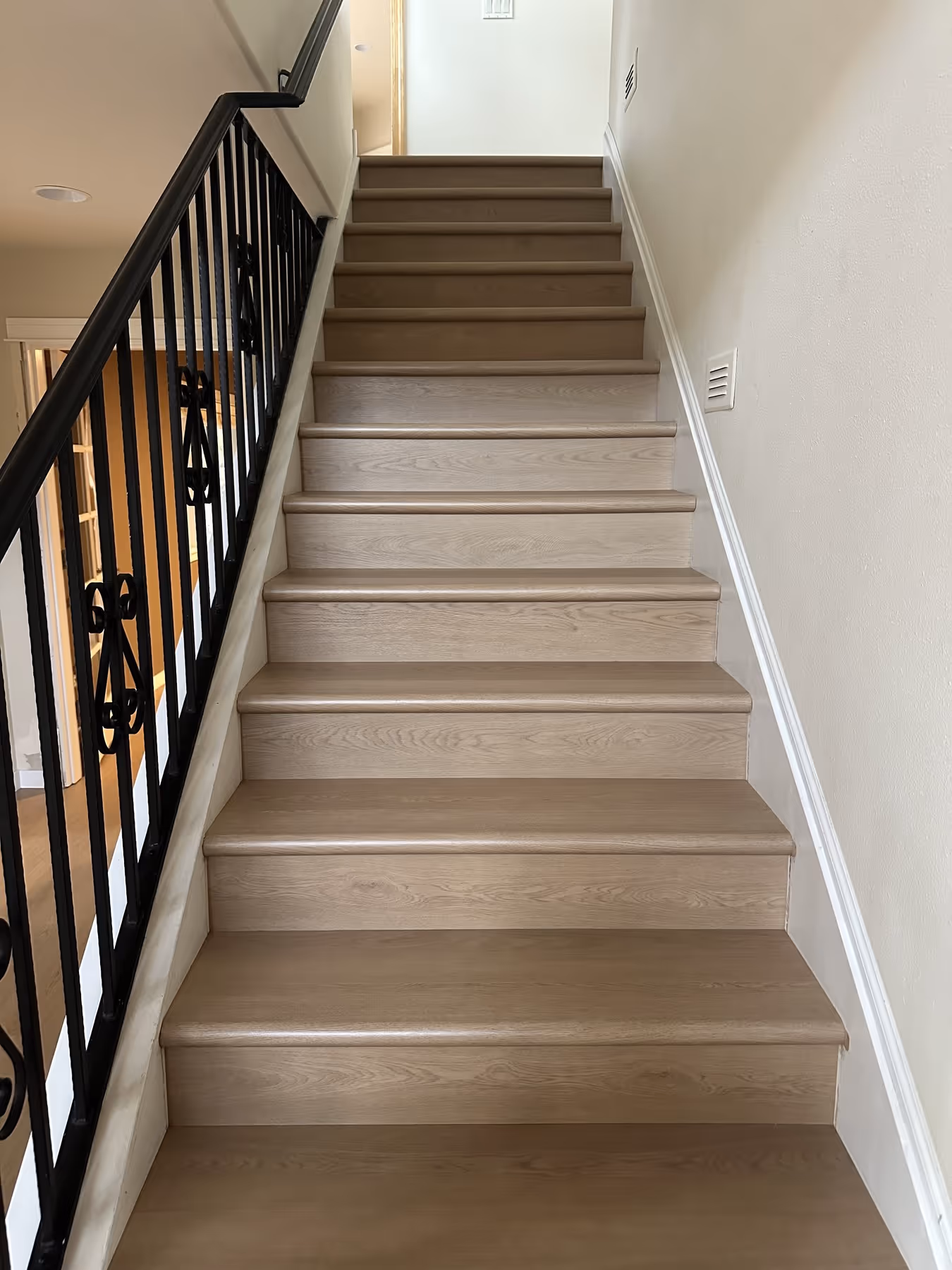 Indoor wooden staircase with light LVP steps and black metal railing on the left side.
