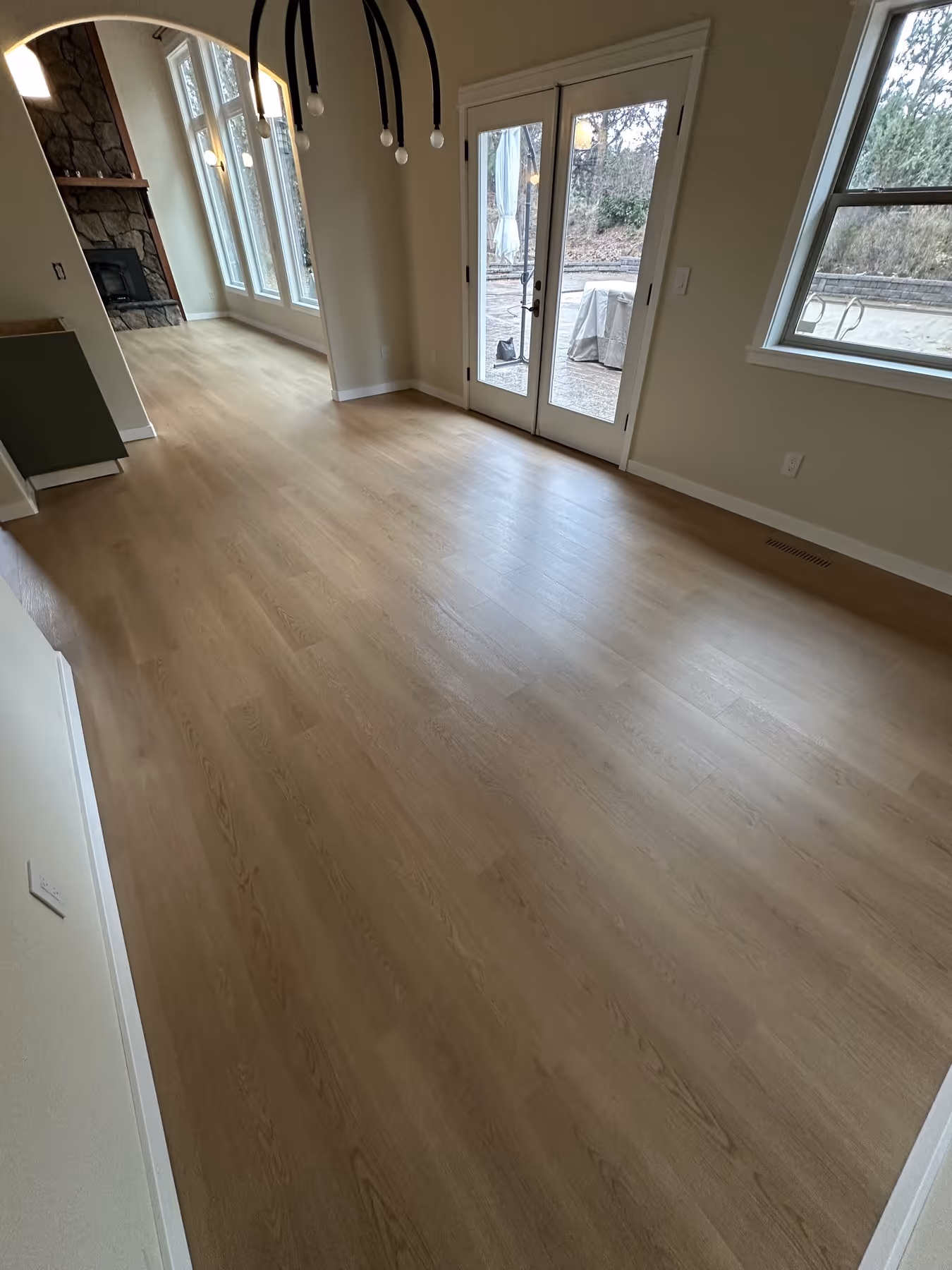 Empty room with light LVP flooring, large windows, a stone fireplace, and glass doors leading outside.