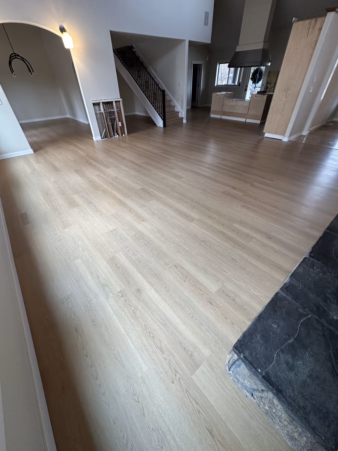 Interior of a home with new light LVP flooring, staircase with black railing, partially finished kitchen, and a stone hearth in foreground.