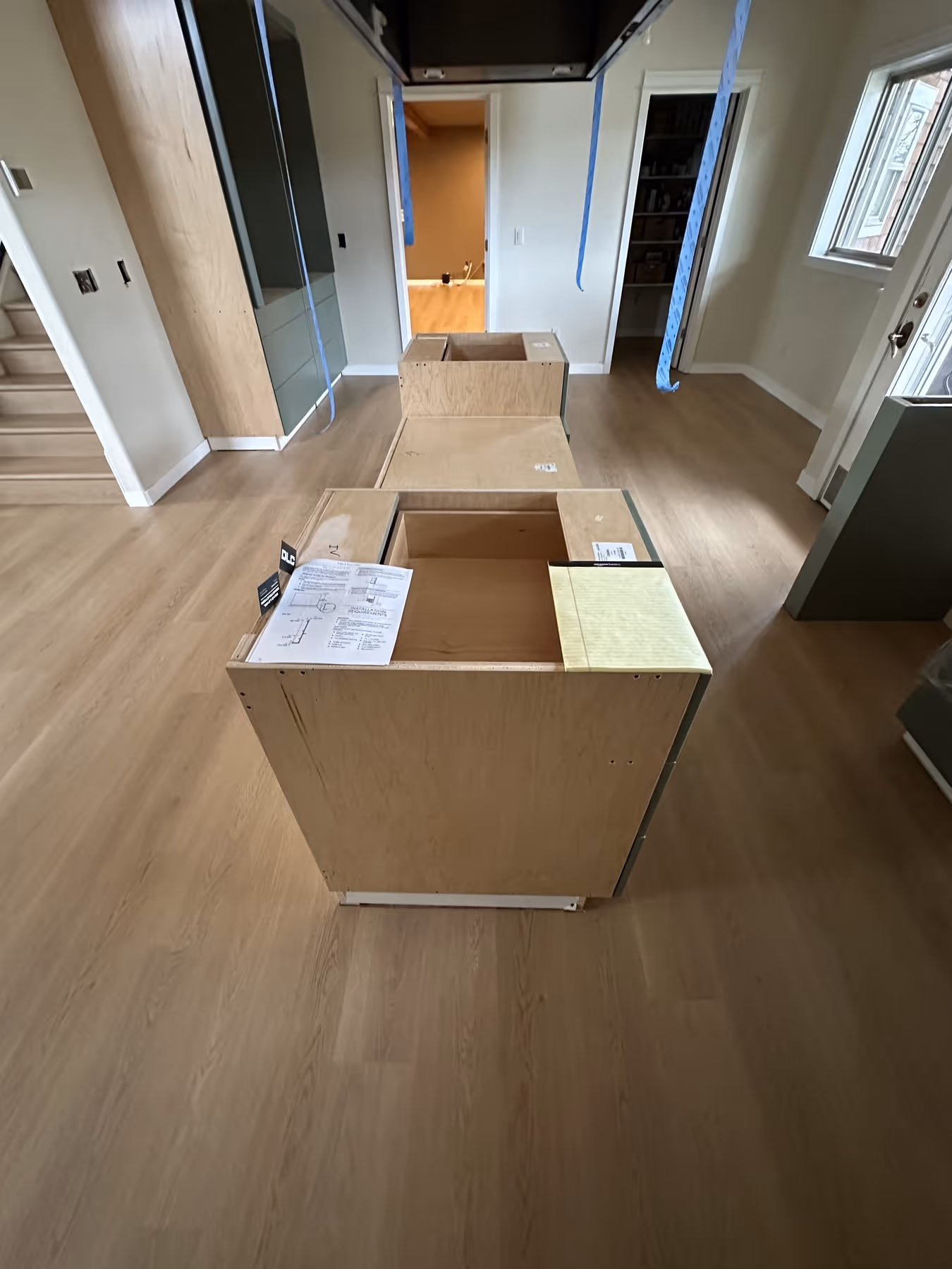 Unfinished kitchen with unpainted wooden cabinets and island in the center on light LVP flooring.