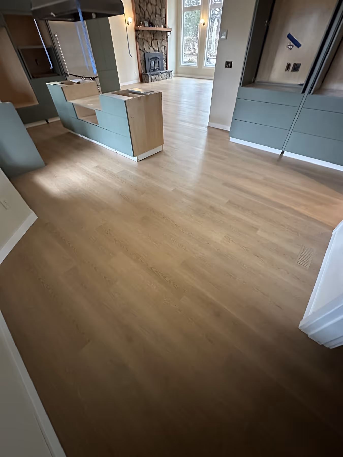 Kitchen interior with light LVP flooring, green cabinets, and a stone fireplace in the background.