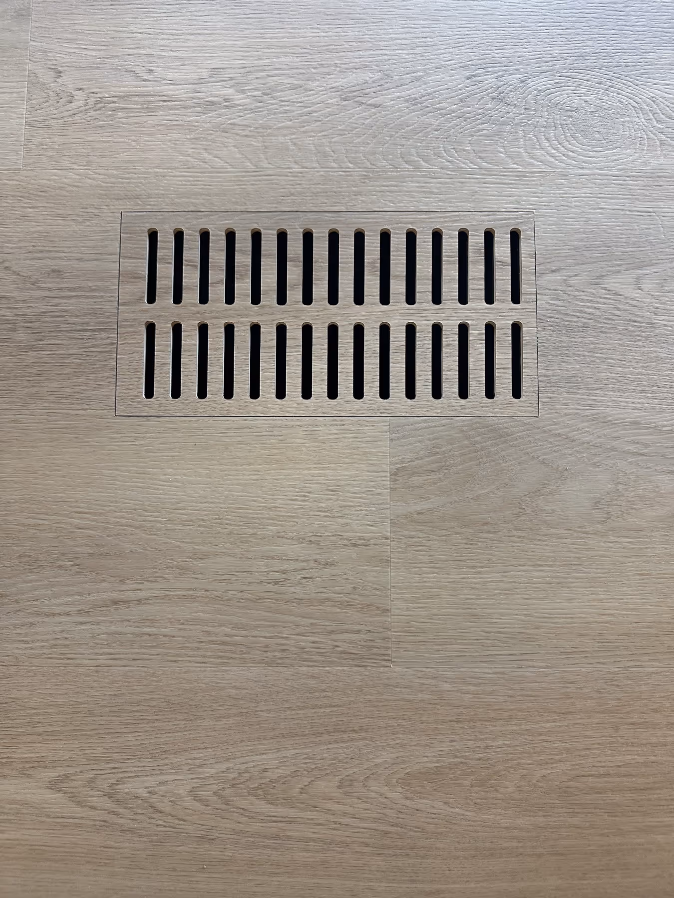 Wooden floor with a rectangular vent cover featuring two rows of vertical slats.