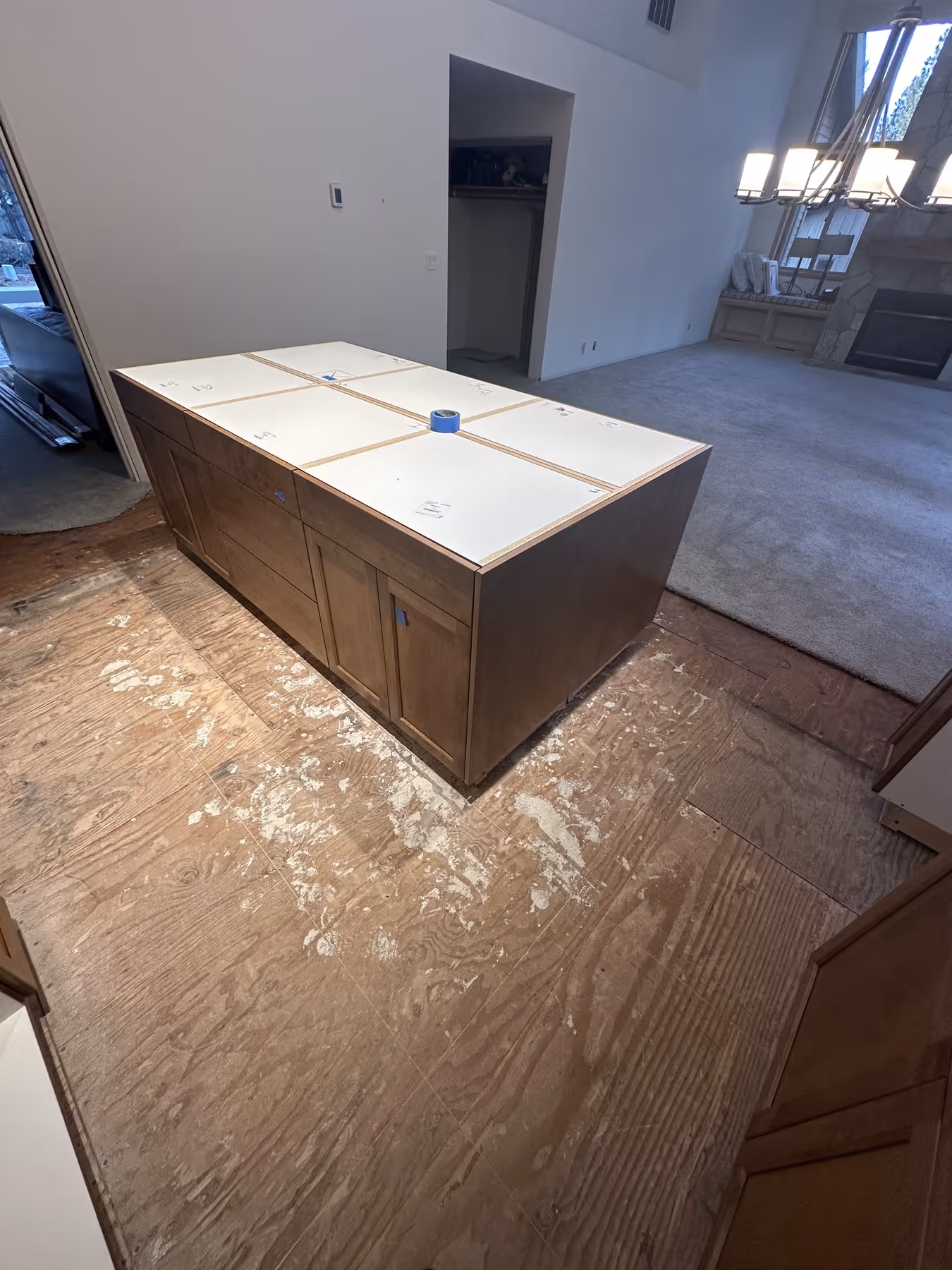 Kitchen island with taped top panels placed on a bare plywood floor in a room under renovation.